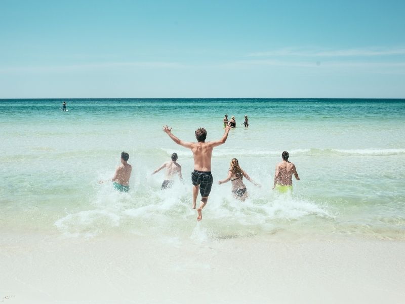 group of beach goers running into the ocean