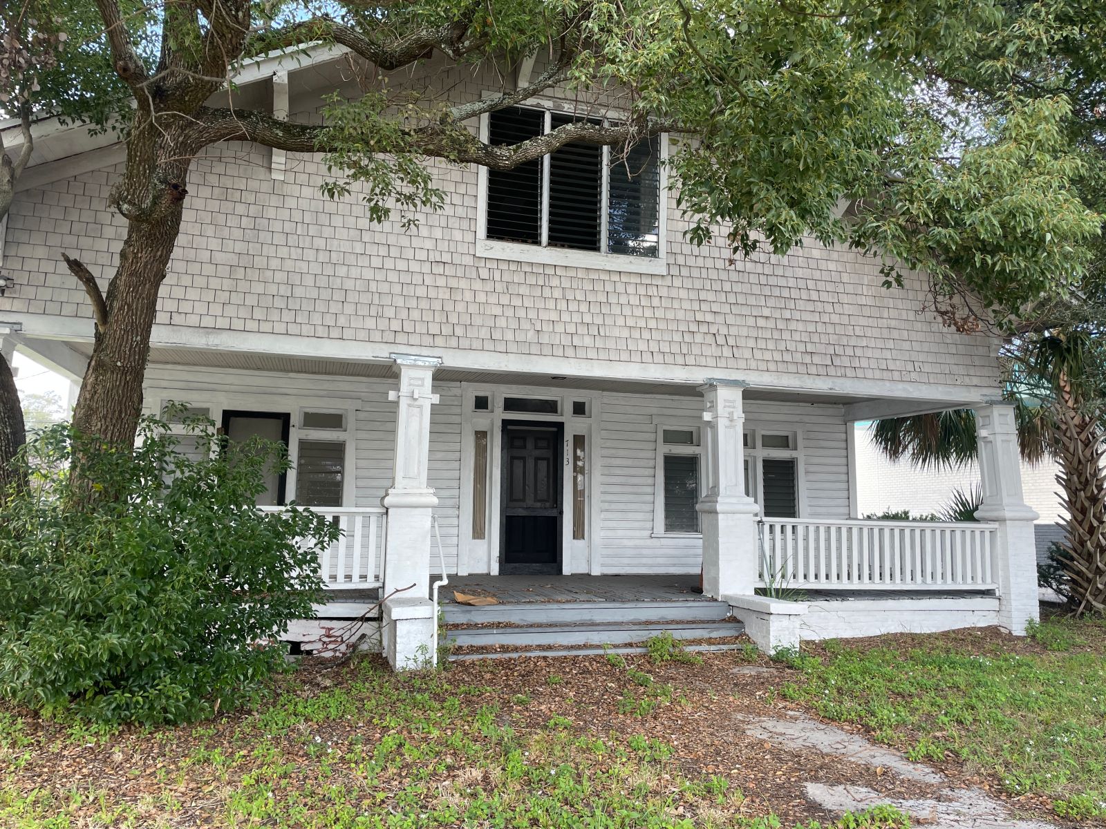 A charming, historic two-story beach house with classic white wood siding, a spacious wrap-around front porch, and large shade trees. This nostalgic architectural style highlights the unique "Old Florida" charm and character-filled accommodations available to guests booking through A Paradise Vacation Rentals on Anna Maria Island.